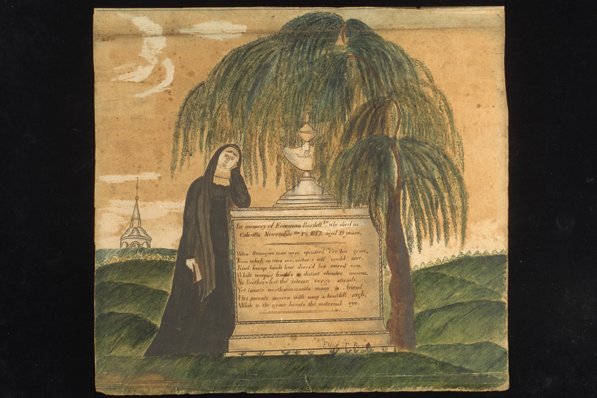 Person in long black dress or gown leaning against a memorial containing text, next to a tree