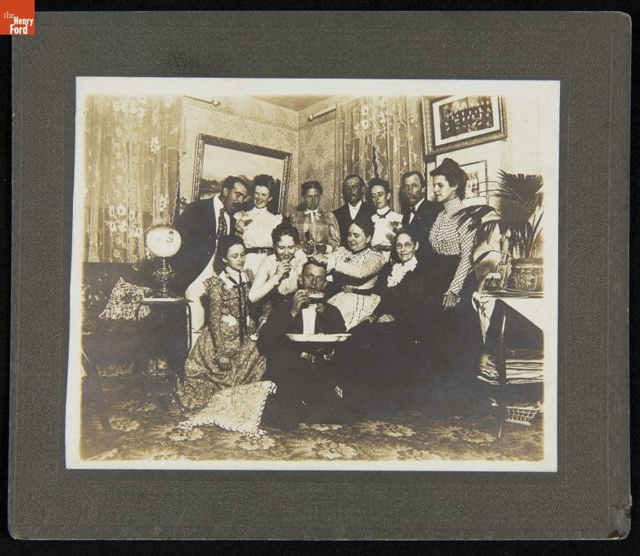 Women and Men at a Gathering Smile and Watch as Another Man Eats Pizza, circa 1900