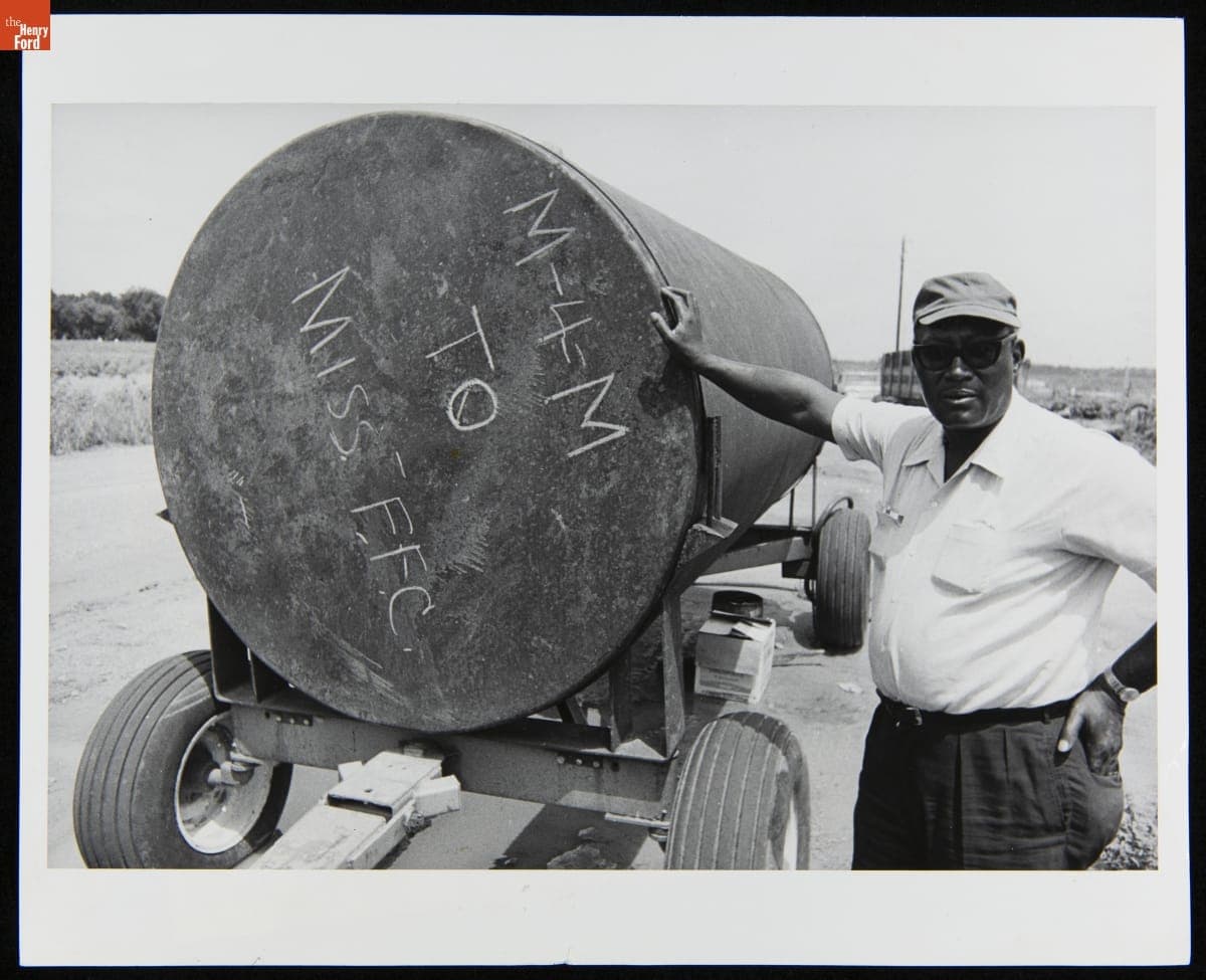 Miles Foster, Farm Manager for Freedom Farms Cooperative, Displaying a Water Tank, December 1972