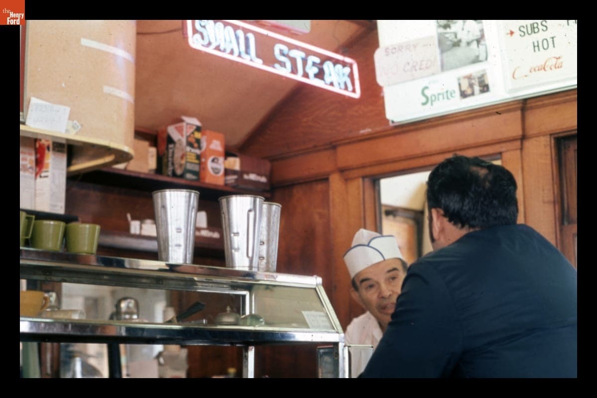 Black & Gold Diner Owner Jimmie Limperopoulis Talking with a Customer, 1973