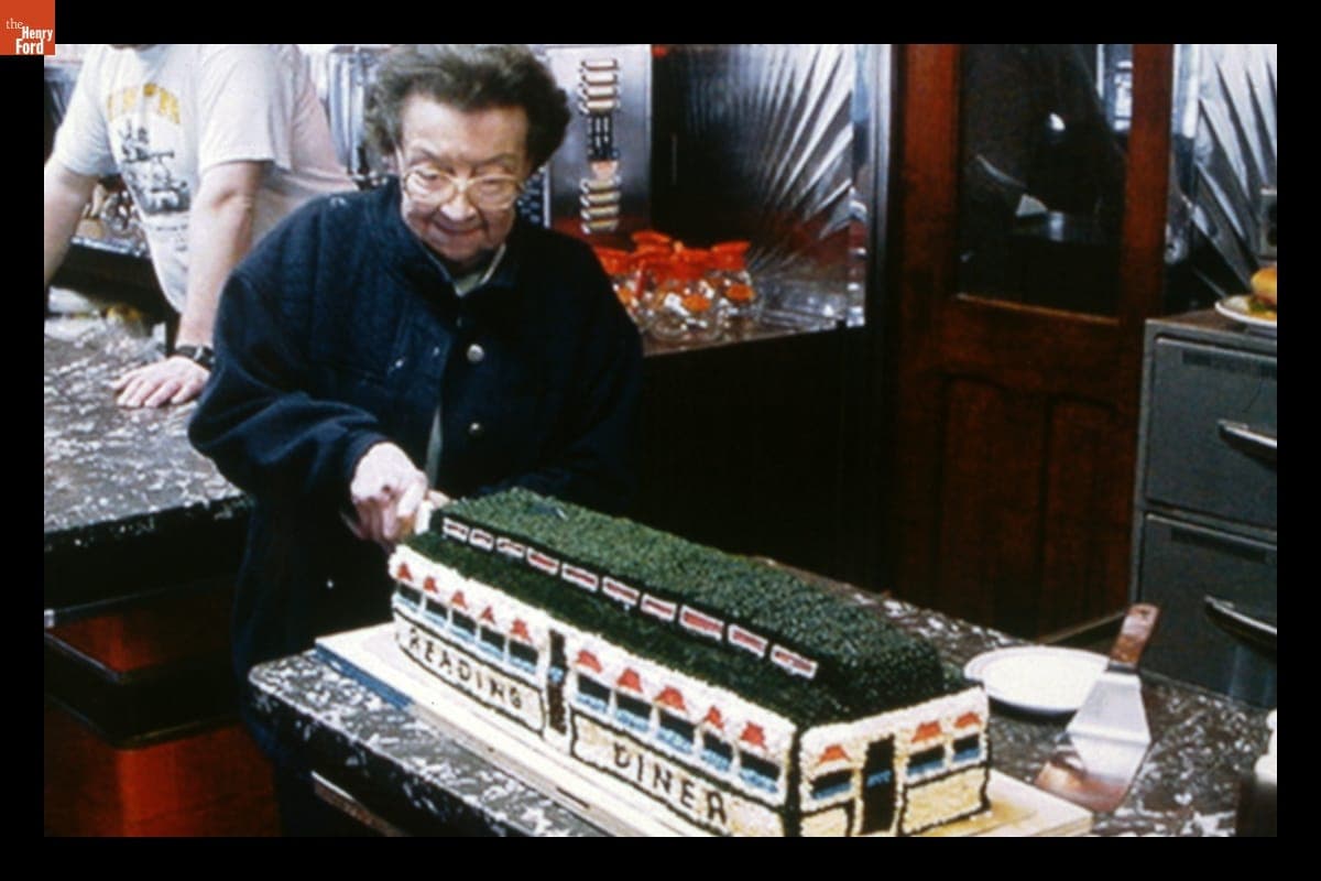 Woman Cutting a Cake Made to Look Like Fegley's Reading Diner