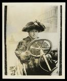 Woman in elaborate fur coat and hat behind the wheel of an open car