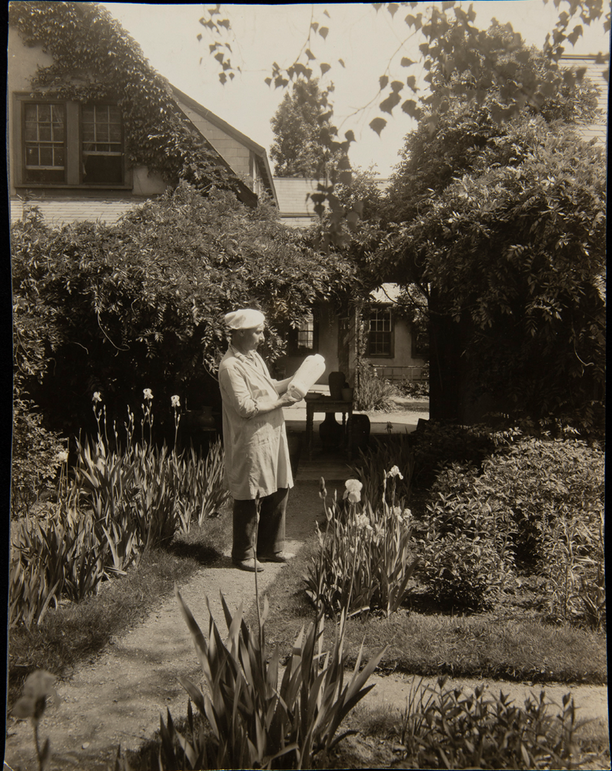 A man holds a piece of pottery in the garden of the Paul Revere Pottery, about 1930