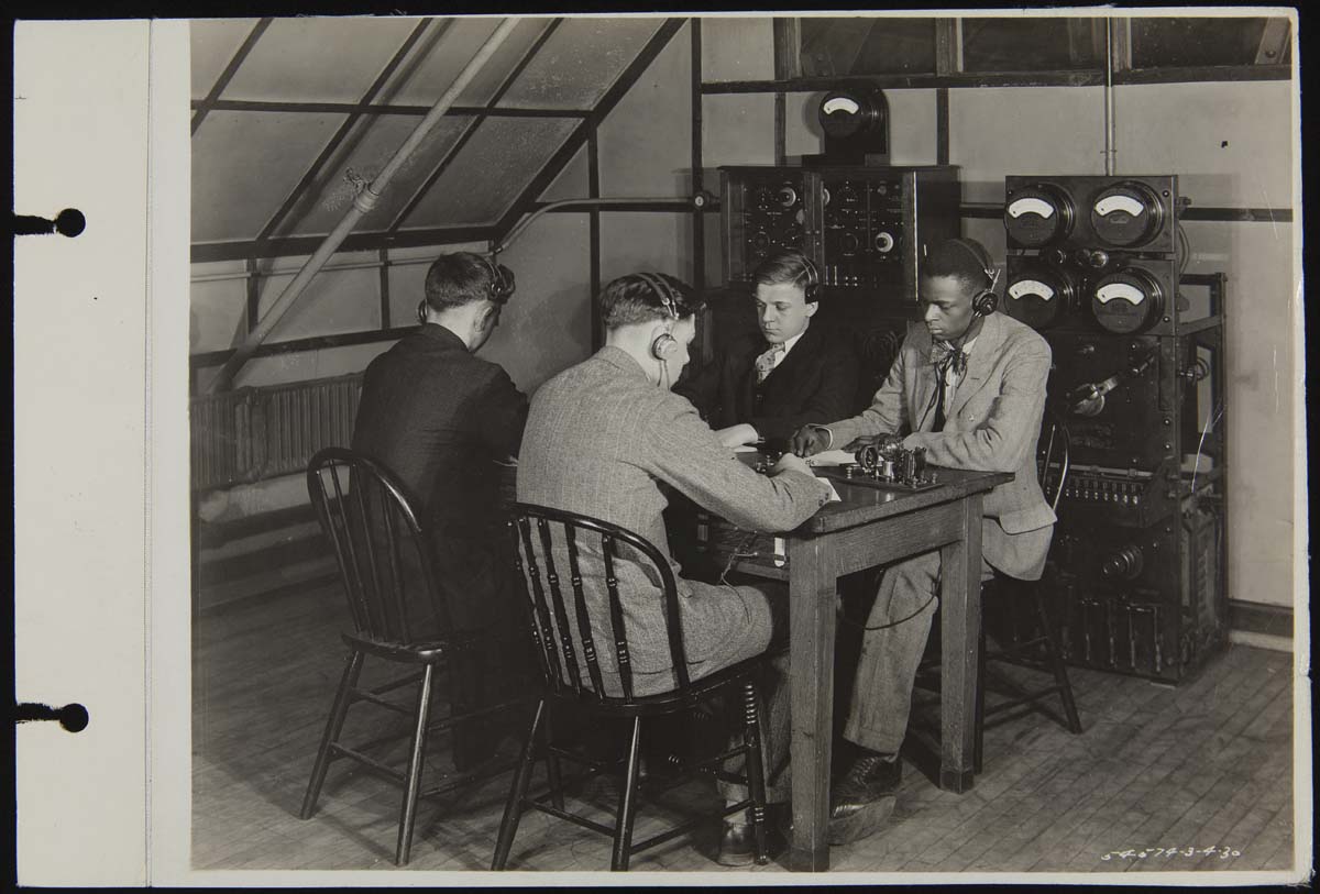 Claude Harvard with Other Radio Club Members, Henry Ford Trade School, March 1930 Four young men wearing headsets sit at a table with machinery, with additional machinery behind them