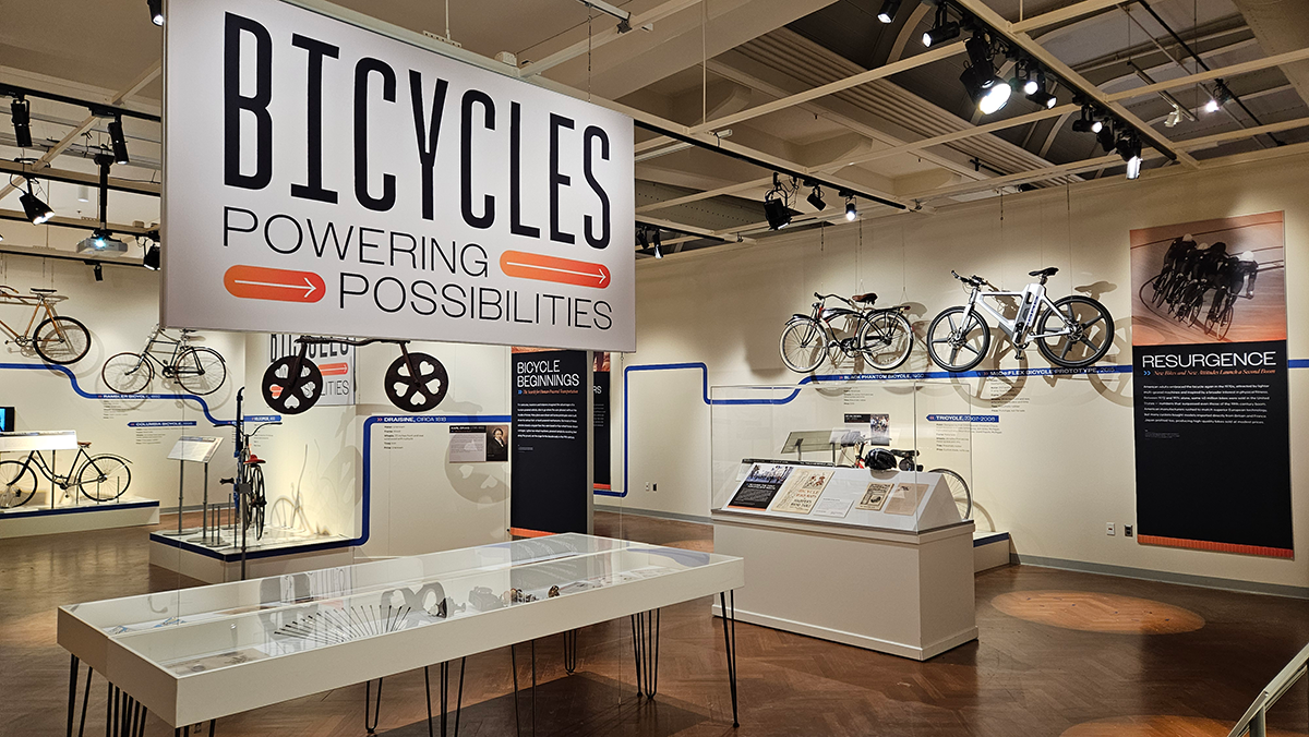 A musuem gallery with display tables and bicycles hanging on the walls