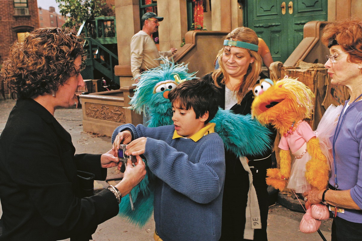 Carmen bringing Rosita to life on the set of Sesame Street Group of people, two holding furry puppets, on TV set designed to look like a street