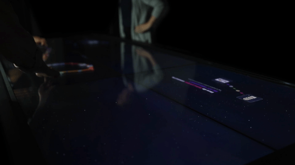Video of people running their fingers over a large touch table, bringing up colorful strings and small images with text