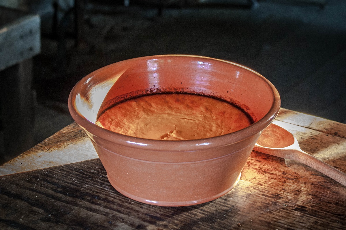 Redware dish containing orange baked pudding, sitting on a wooden table
