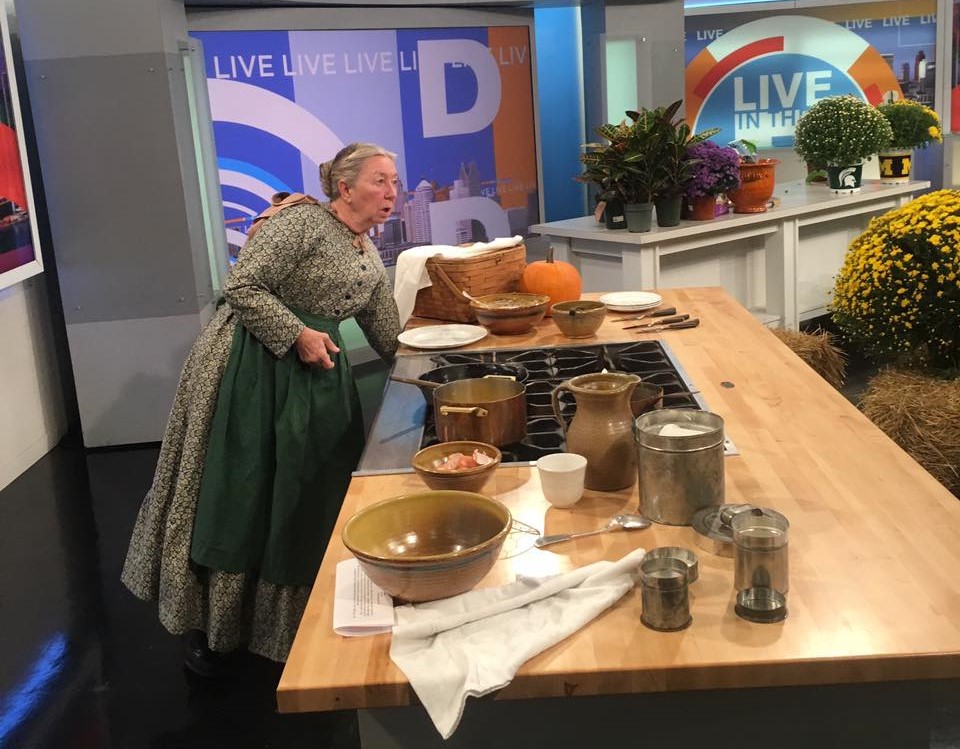 Woman in old-fashioned dress and apron cooks on a television soundstage