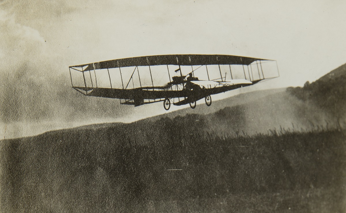 Black-and-white image of early glider in air over a wooded area