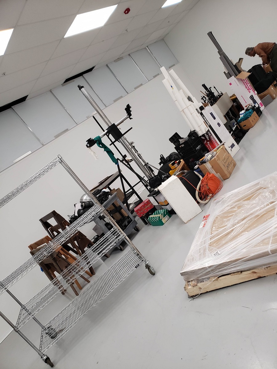 Angled photo of furnishings and equipment lined up in a clump in the middle of a white room