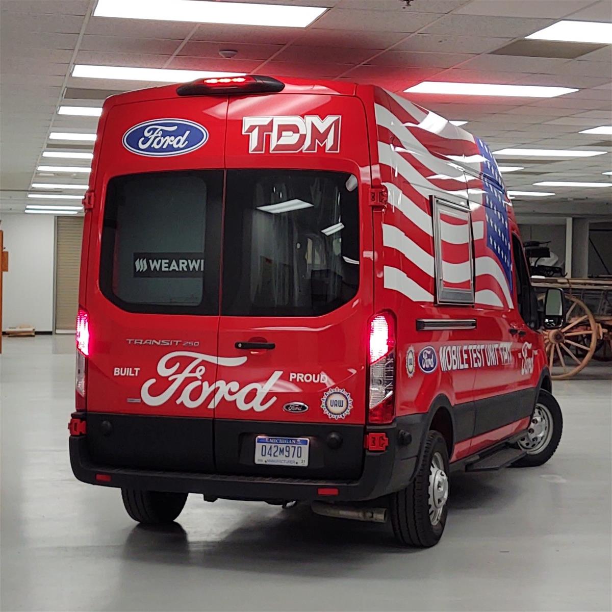 Ford Transit Van, Modified for Use as a COVID-19 Mobile Testing Facility, 2020 Rear view of red van with large back window; various text on vehicle and large American flag on visible side