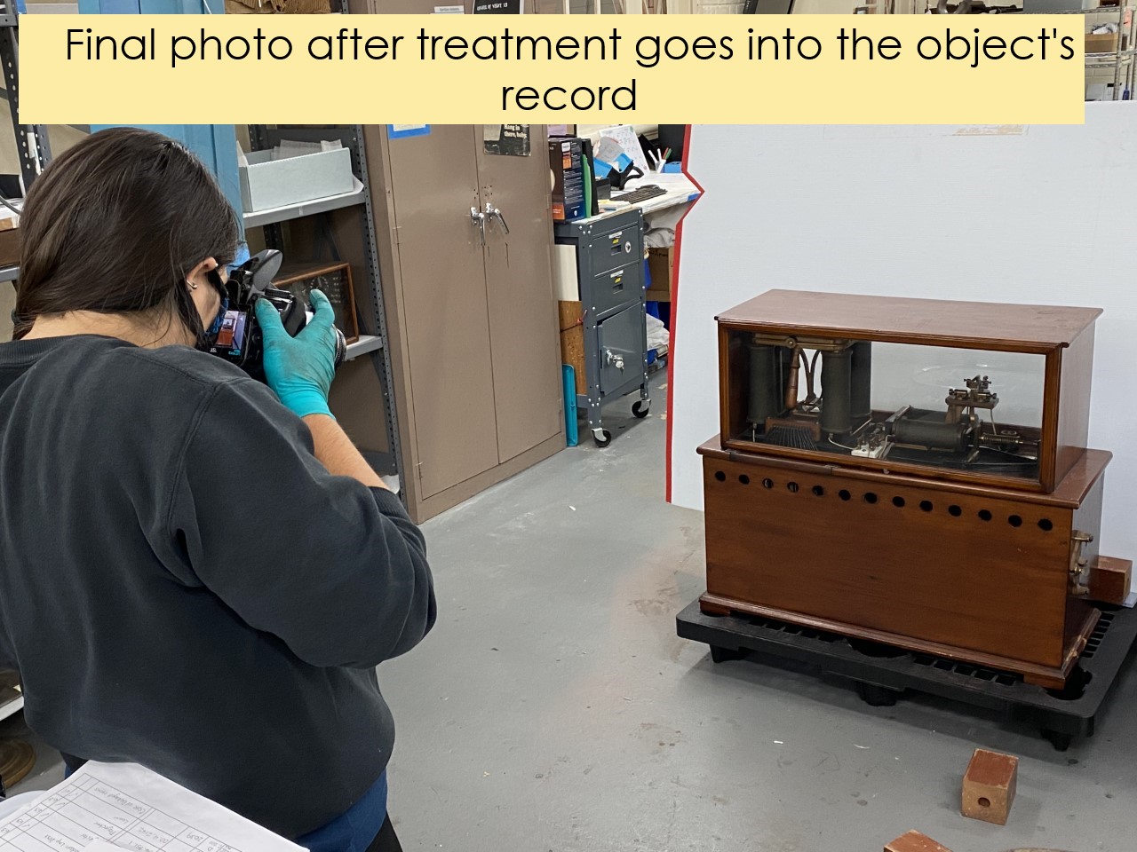 Person in gloves photographing a wood cabinet with machinery inside