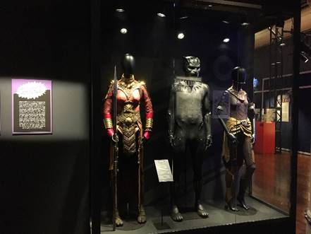 Three mannequins in costumes in case with text panel to left