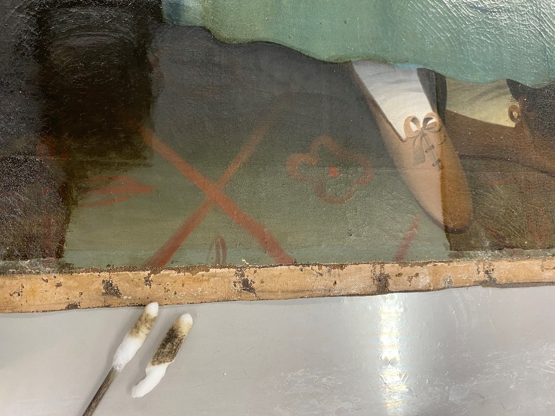 Bottom of painting canvas showing floor and shoes, with one portion lighter than the remainder; tools nearby