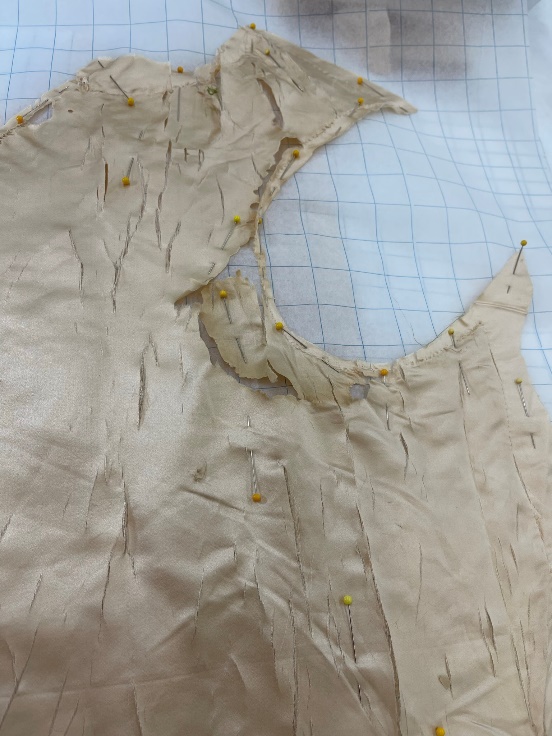Pattern making from the shattered silk lining Cream silk fabric with many rips and gaps lays on top of gridded paper