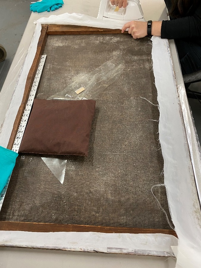 A person's hands work at top of painting laid facing down on flat table