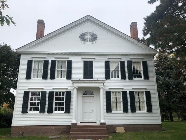 Two-story white wooden house with symmetrical windows with black shutters and a peaked roof