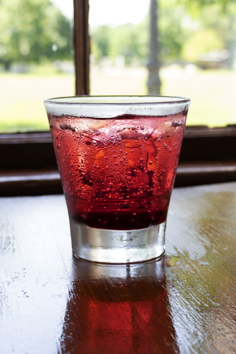 A nonalcoholic Cherry Effervescing, as served at Eagle Tavern in Greenfield Village Red-colored drink with ice in glass sitting on wooden table by window