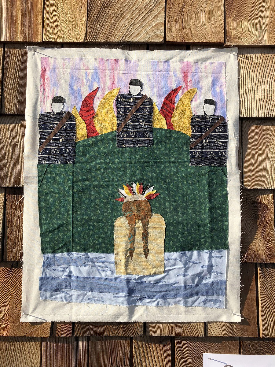 Block made by SJSA participant Autumn Roberts about the Dakota Access Pipeline protest Fabric block depicting a figure wearing feathers on head in water, while three figures in black with bandoliers or sashes look on from a flame-topped hill
