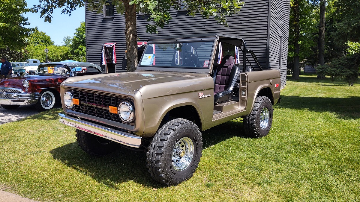 Copper-colored Jeep-like vehicle parked among other vehicles in front of a gray wooden building