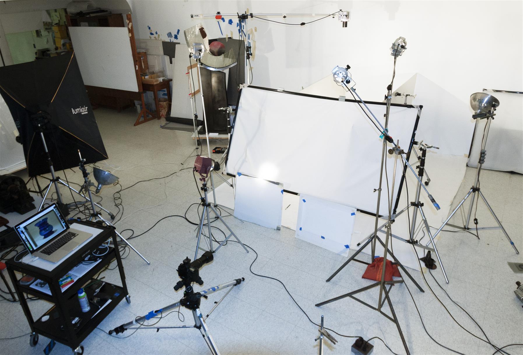 Photo studio with cart with laptop, many lights on stands, area blocked off with white paper