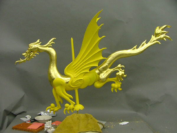Bright gold, partially shiny and partially dull, figure of dragon with tools and implements nearby