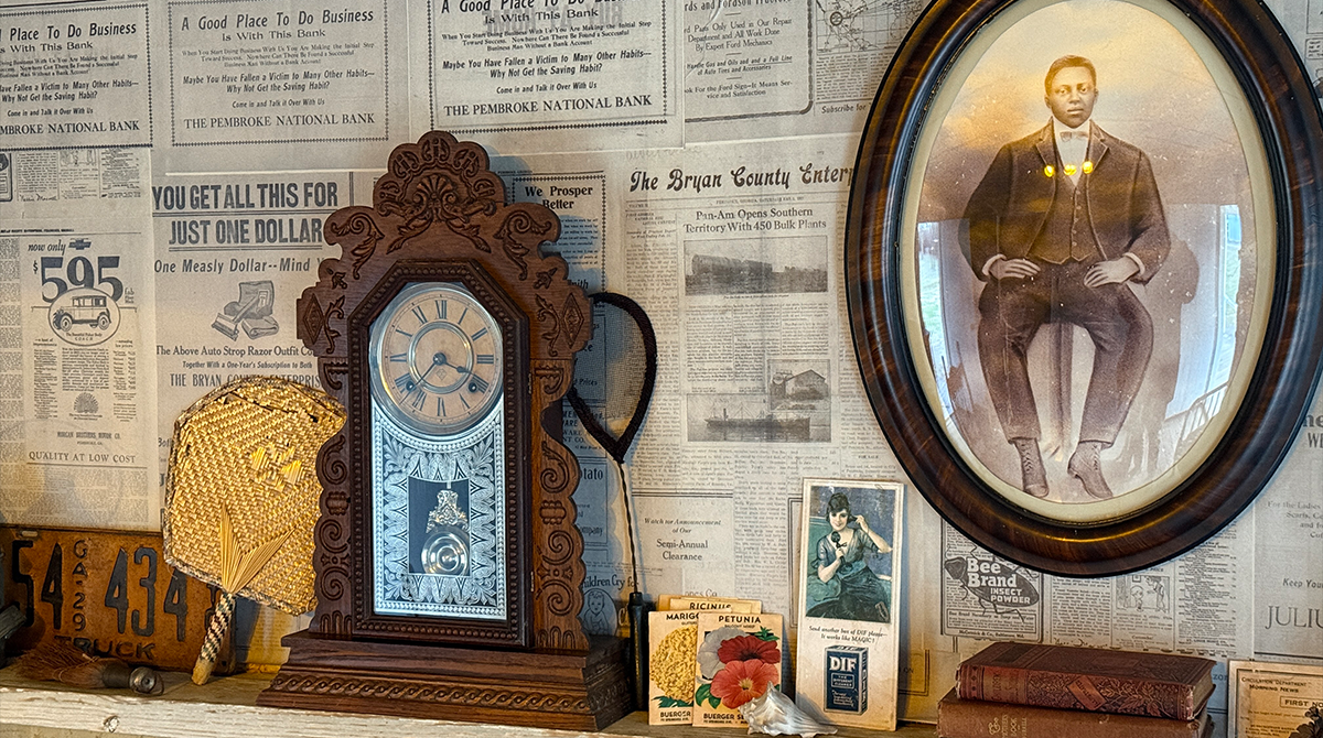 A wooden clock and framed photo of a man in front of a wall covered in wallpaper