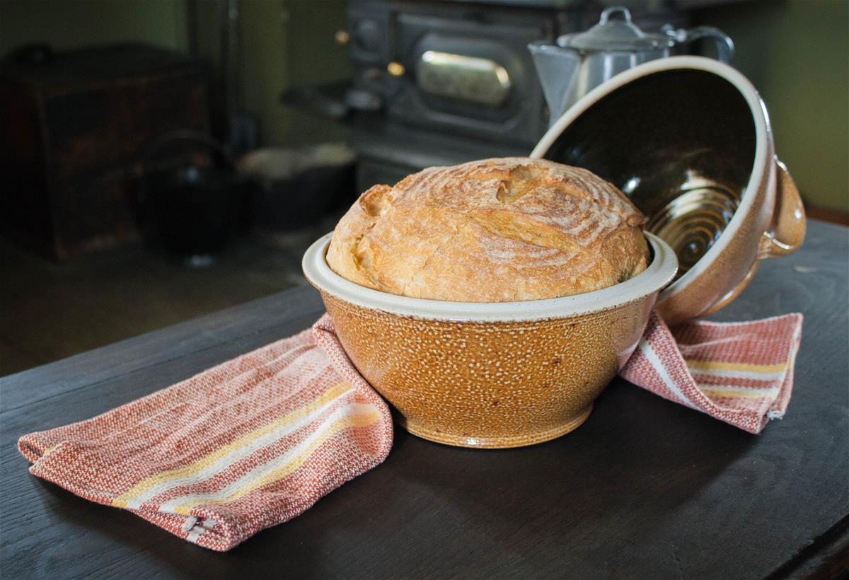 Bread in a mustard-colored stoneware bowl with lid and red-and-white dishtowel nearby