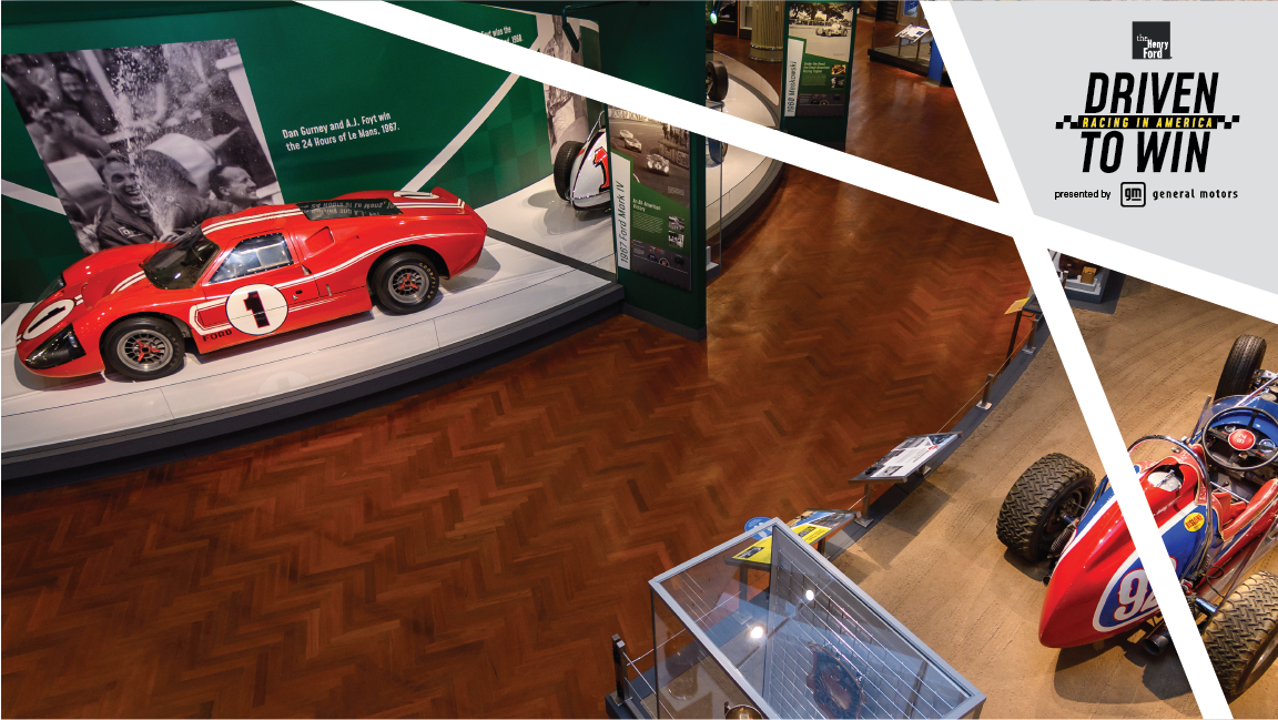 Aerial view of museum exhibit featuring low red race car with number 1 in circle on side and hood, along with red and blue open race car