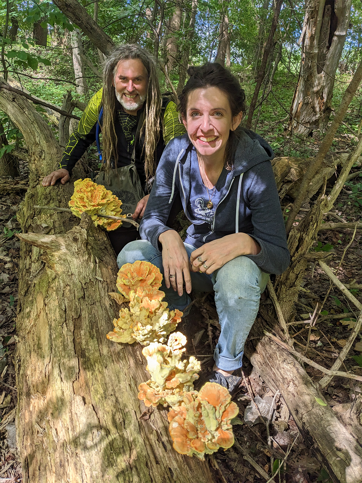 nick-king_erin-hamilton Nick King and Erin Hamilton sit on a log alongside several yellow and orange mushrooms