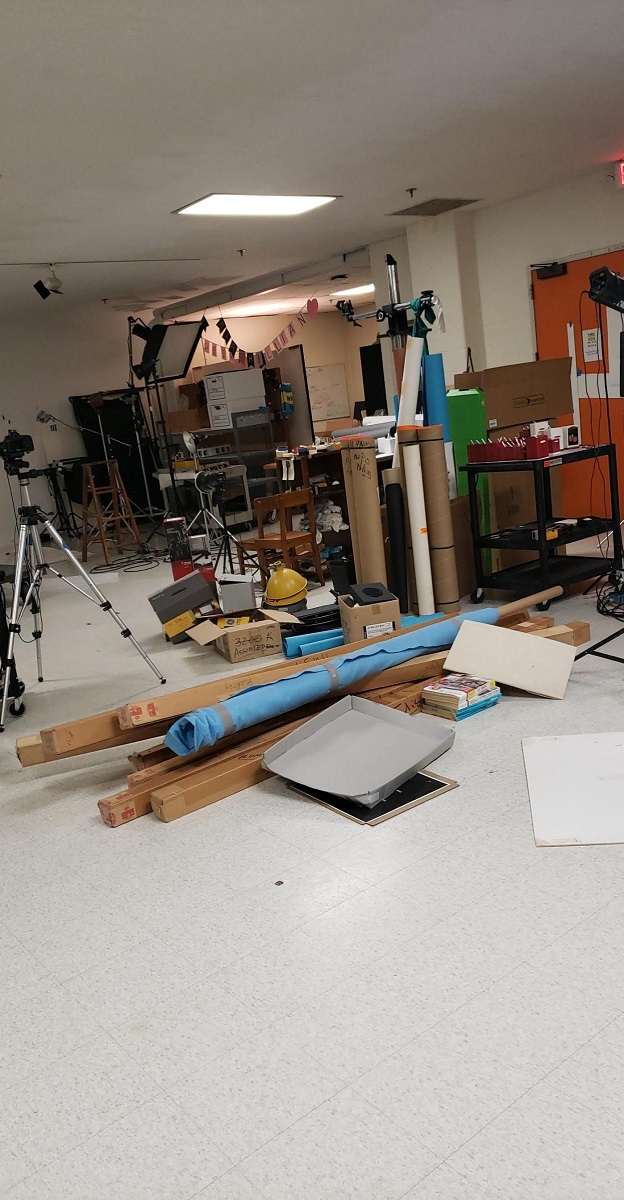 Room cluttered with rolls of material, boxes, and other items in a pile on the floor