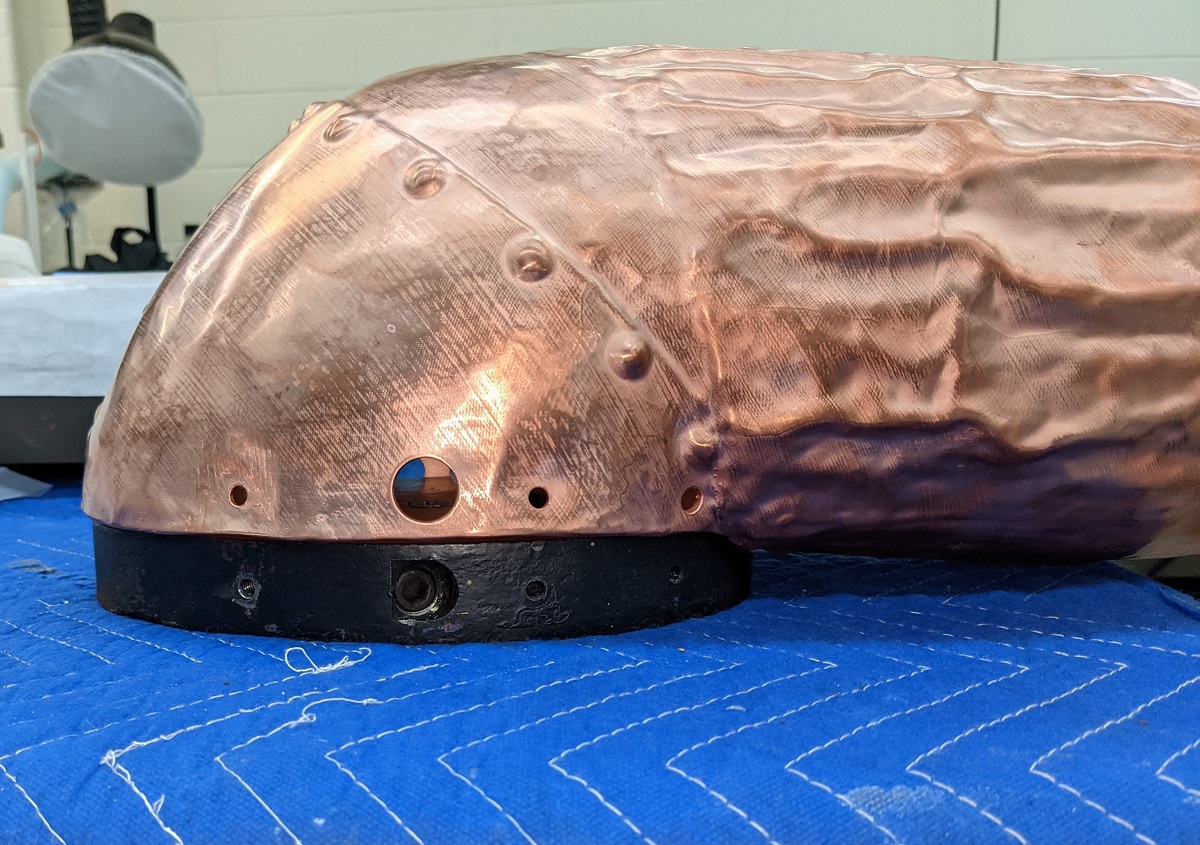 Holes in the cast iron mount for the arm Copper form with black base sitting on blue quilted fabric