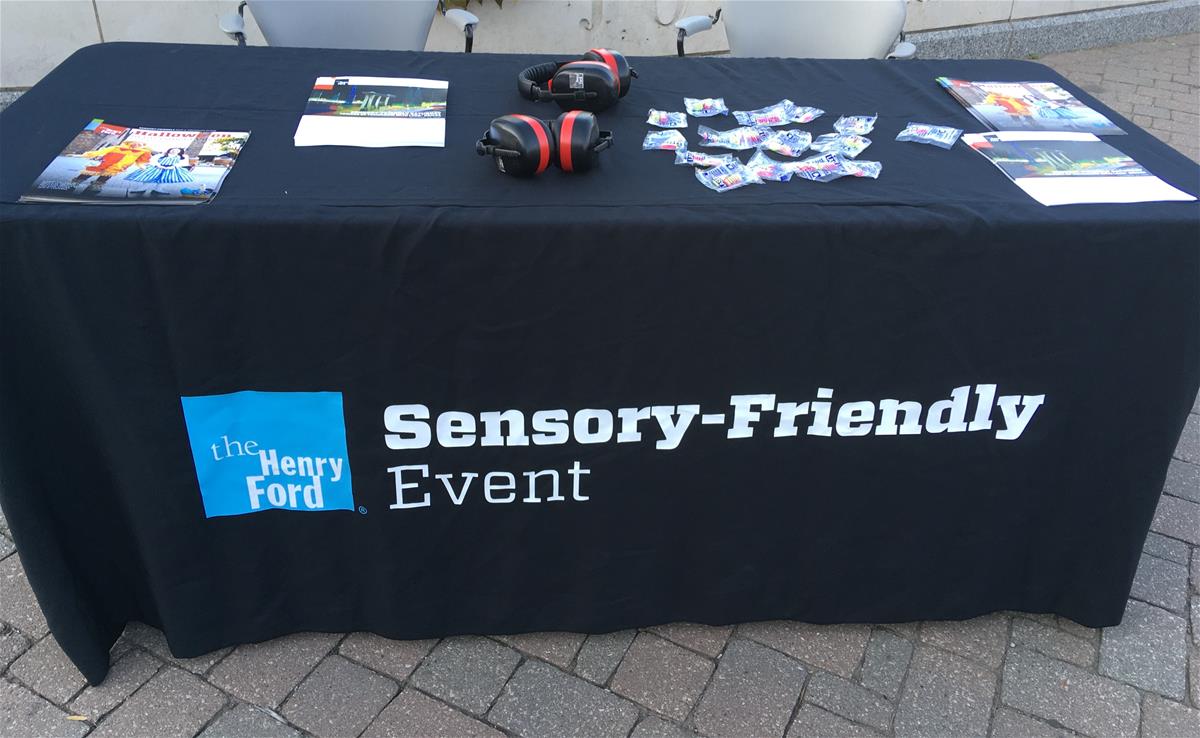 Table covered in black cloth with text "Sensory-Friendly Event" and brochures and headphones on top