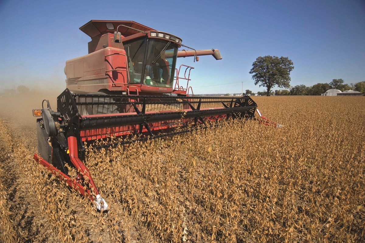 A large red piece of farm equipment moves through a field of brown plants