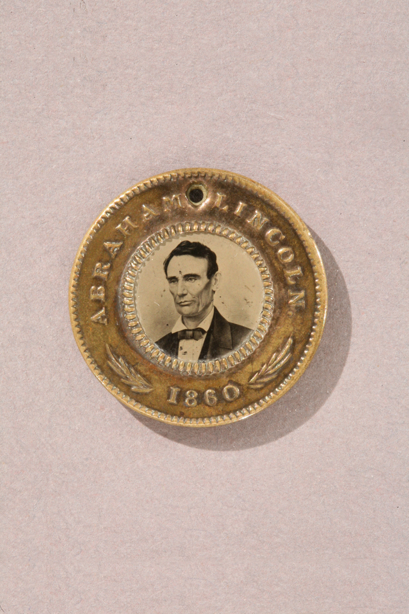 Gold colored button with text "Abraham Lincoln 1860" and portrait of man in center