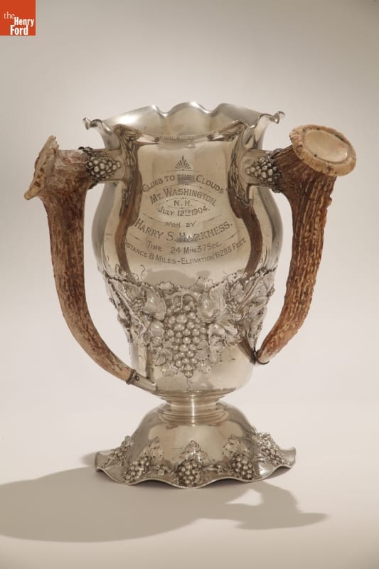 Silver vase-shaped trophy with text and pattern of grapes, and handles made out of antlers