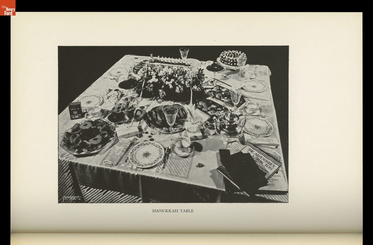 Image labeled "Hanukkah Table" of decorated table with place settings, food, books