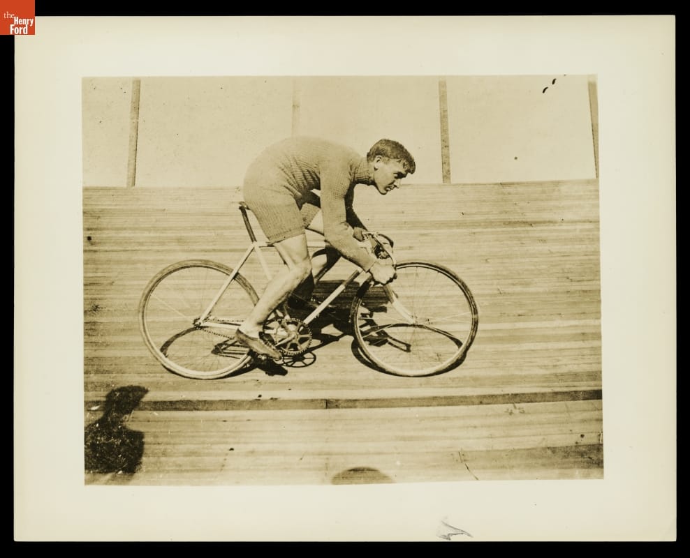 Barney Oldfield Riding the "Blue Streak" Bicycle on the Salt Palace Board Track, Salt Lake City, Utah, circa 1900 Man hunched over riding a bicycle on a steeply-tilted wooden track