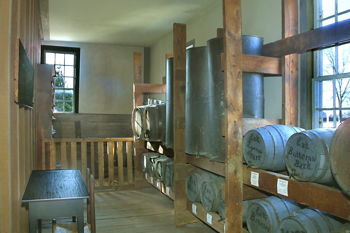 Narrow room with built-in racking filled with casks and vats labeled with hand-written text
