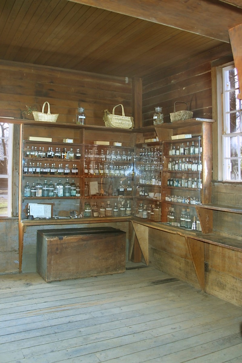 Corner of room with wooden floors and walls covered with narrow shelving containing many bottles and jars