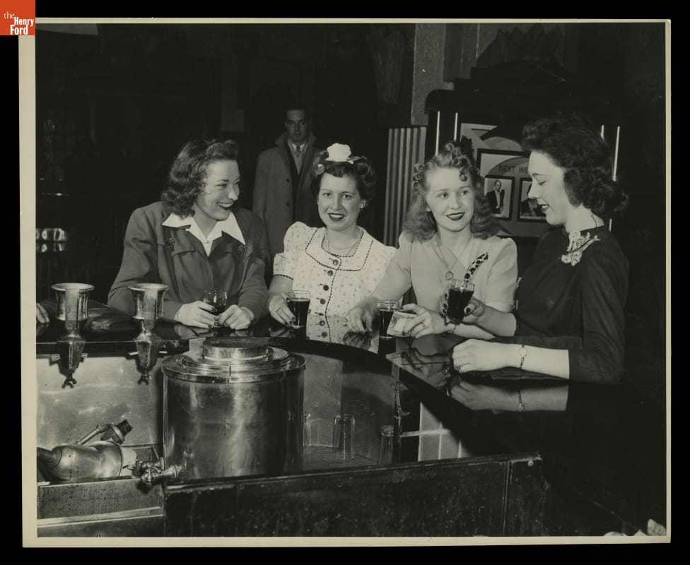 Four women with beverages sit at a counter