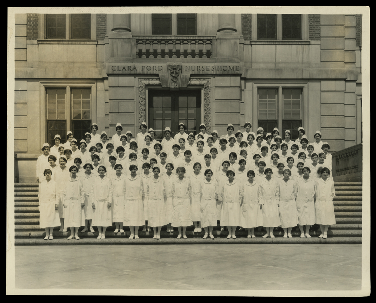Group of women in nurses' uniforms stand on the steps of a building inscribed 