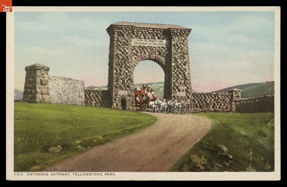 Entrance Gateway, Yellowstone Park, 1903-1904 Postcard showing large stone gateway across dirt road through grass fields; a horse-drawn stagecoach is coming through the arch