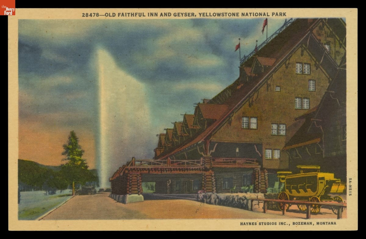 Postcard showing side and sliver of front of large, steeply-roofed rustic building with a geyser erupting in the background