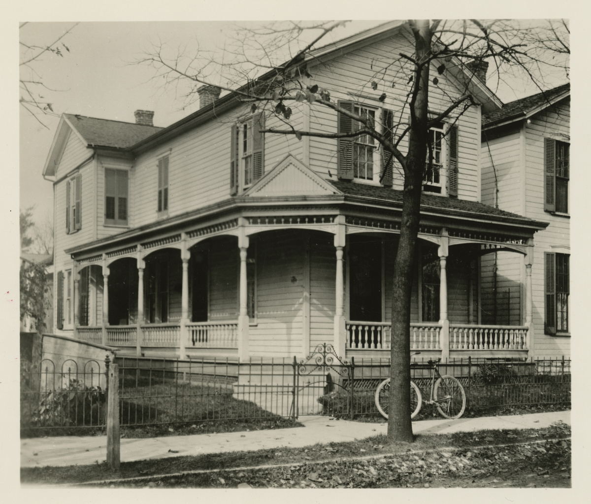 Outside view of two-story house with wrap-around porch and bicycle propped against fence