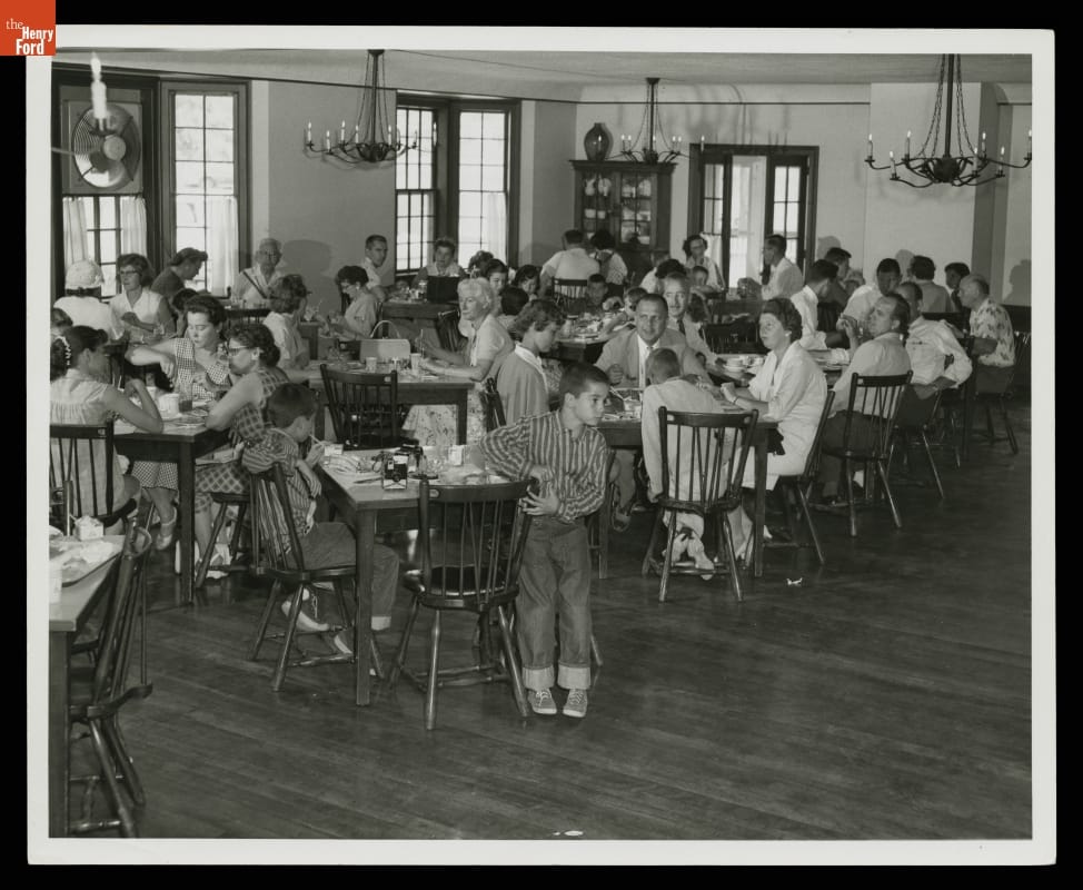 Room filled with people eating at small square tables