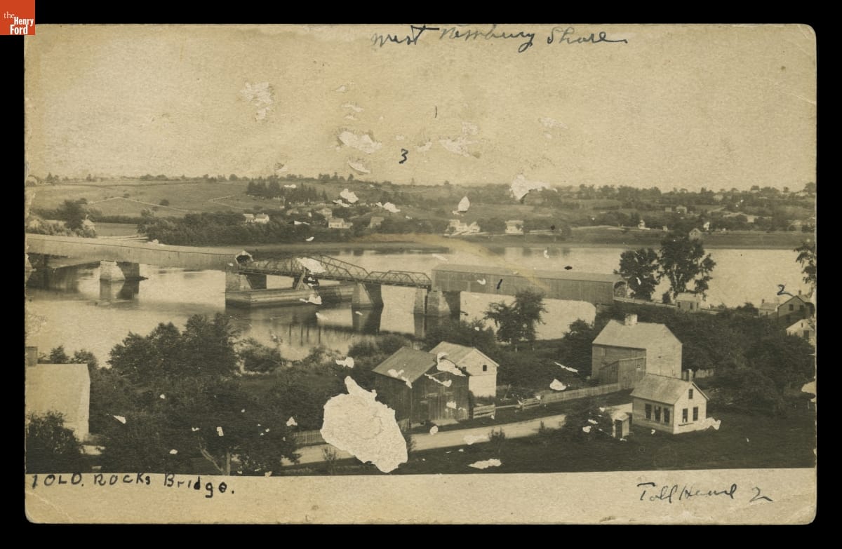 Old Rocks Bridge, East Haverhill, Massachusetts, Showing Rocks Village Toll House, circa 1910 Body of water with buildings on either side and a bridge across