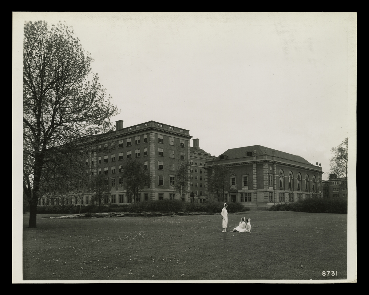 Large five (?) story brick building, with three people in nurses' outfits on the lawn in front
