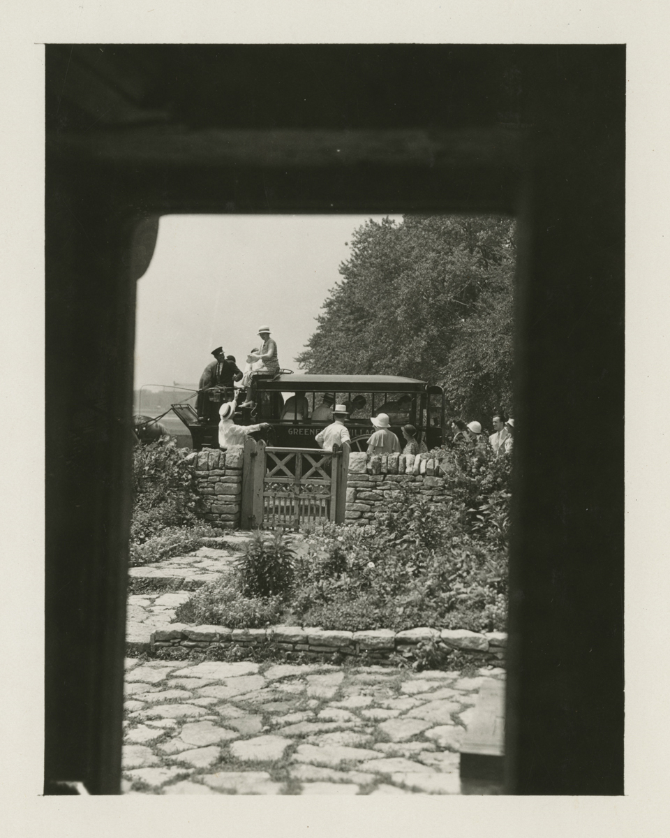Visitors in Horse-Drawn Omnibus at Cotswold Cottage in Greenfield Village, June 7, 1933 Photo taken from inside a window of people dismounting from an omnibus outside a garden with a gate